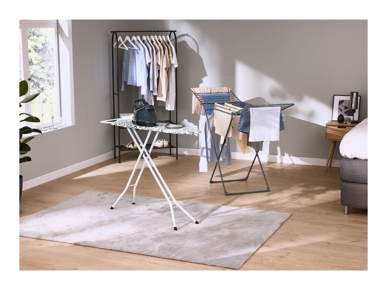 An ironing board with an iron and a clothes drying rack in a modern bedroom.