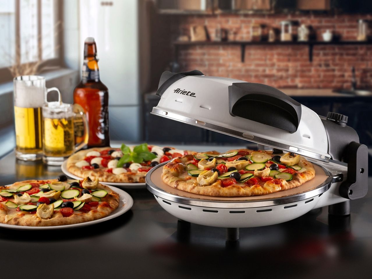 Un forno per pizza Ariete con una pizza vegetariana e due pizze aggiuntive, con birra sullo sfondo.