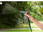 Hand holding a PARKSIDE® garden hose set, spraying water in a garden.