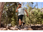 Homem com t-shirt CRIVIT e calções pretos a caminhar numa floresta.
