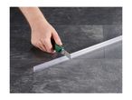 A hand cutting a transparent shower door seal with a utility knife on a dark tiled floor.