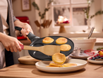 Жена прехвърля палачинки от тиган за палачинки в чиния, докато приготвя закуска.