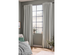 Cortinas Livarno® cinza claro numa janela grande com poltrona e manta.