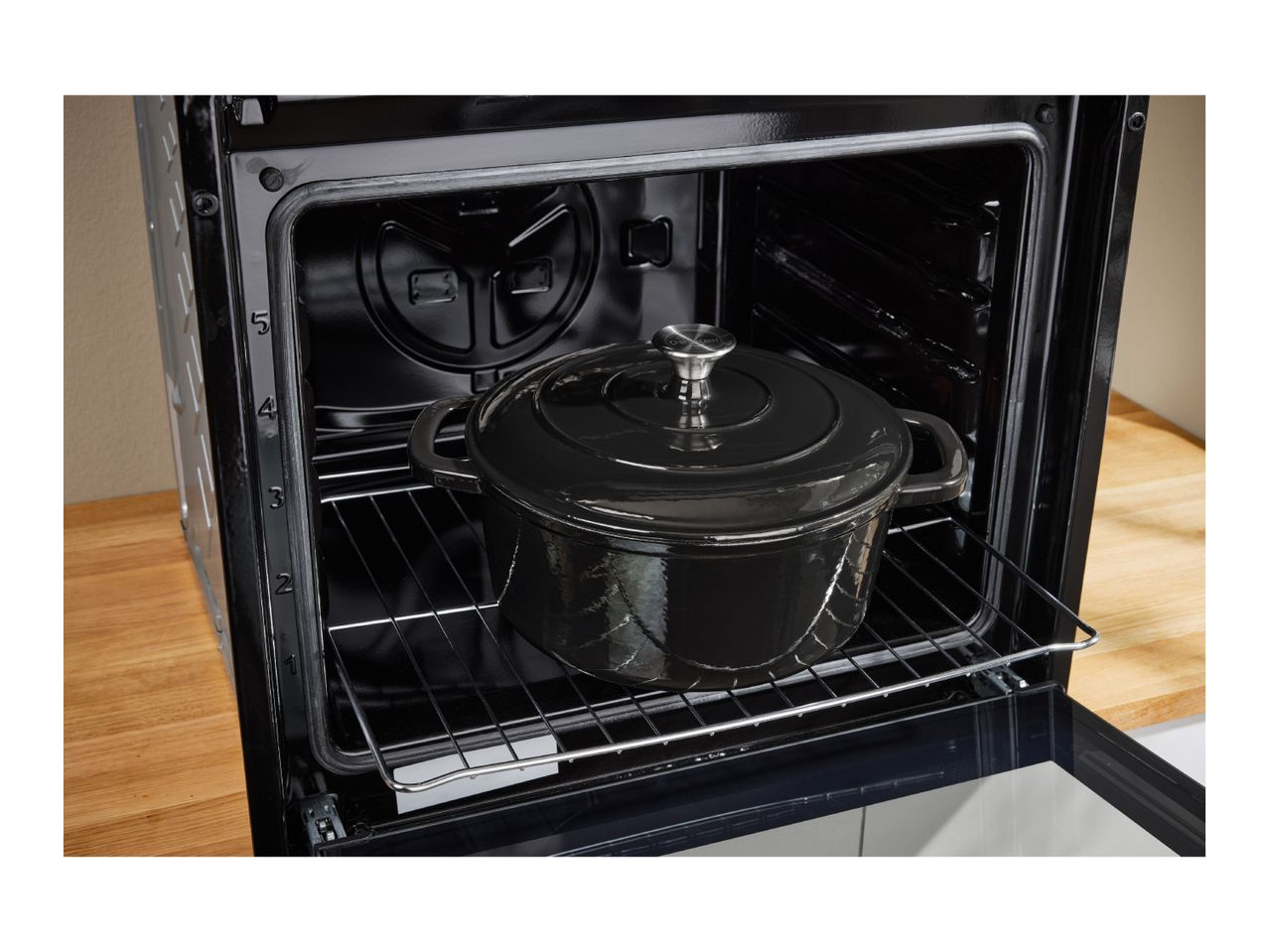 A black cast iron pot with a lid inside an open oven on a rack.