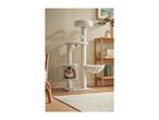 A cat tree with a cat inside, next to a wooden shelf with books and a plant.