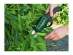 Hands using electric pruning shears to trim green leaves on a bush.