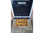 An autumn-themed doormat with leaves and 'ABHAILE' text in front of a black door.
