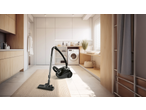 Black cylinder vacuum cleaner on a beige rug in a modern laundry room.