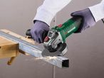 A person wearing gloves uses a green and black angle grinder to cut a metal beam.