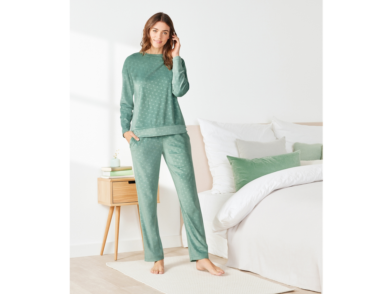 Femeie în pijama Esmara din velur cu buline, stând lângă un pat.