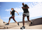 Two runners in black activewear and running shoes, exercising outdoors under a blue sky.