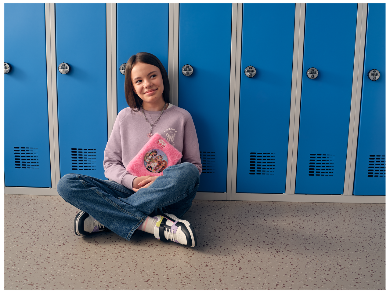 Une jeune fille assise devant des casiers bleus, tenant un journal rose moelleux.