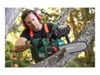 Man wearing safety gear, cutting a tree branch with a chainsaw, sawdust flying.