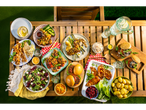 A vibrant summer picnic spread features grilled meats, burgers, salads, and sides on a wooden table.
