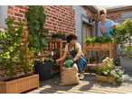 Two women gardening on a patio, one wearing Parkside® Gardening Gloves, planting from a burlap sack.