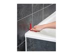 Hand using a red caulking tool to smooth sealant around a white bathtub edge against dark tiles.