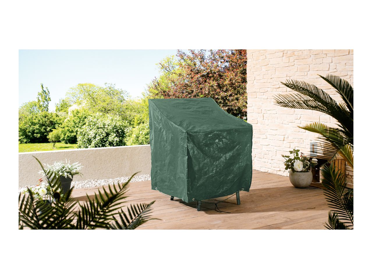 Green protective cover on a garden chair on a wooden patio with plants and trees.