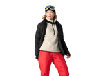 Woman in black ski jacket, cream fleece, red ski pants, and ski goggles.