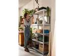 Woman organizing metal shelving with tools and plants.