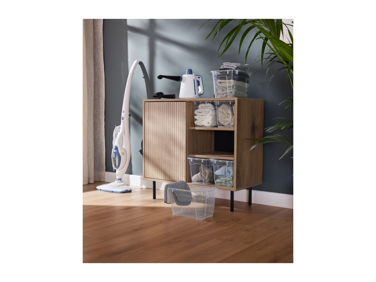 Steam mop and handheld steam cleaner next to a wooden cabinet with clear storage boxes.