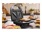 Sandwich maker with a toasted sandwich and ingredients on a kitchen counter.