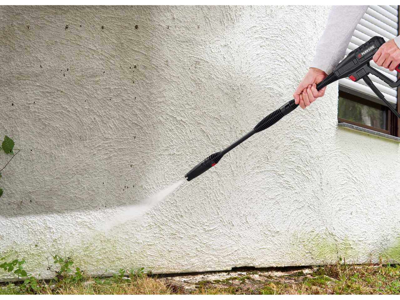 A person cleans a wall with a Parkside pressure washer.