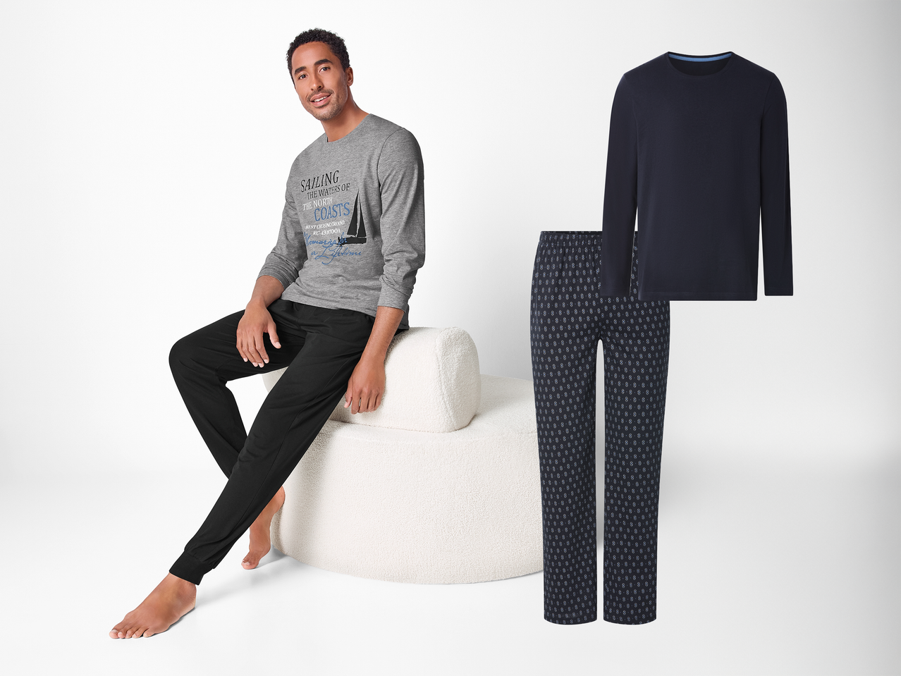 Moška pižama s sivo majico z dolgimi rokavi z motivom jadranja in črnimi hlačami, poleg pa je še temno modra pižama z vzorcem.
