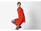 A woman in an orange Esmara ladies' jumper dress and black tights sits on a clear stool.