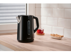 Black electric kettle on a wooden countertop with tea and cookies.