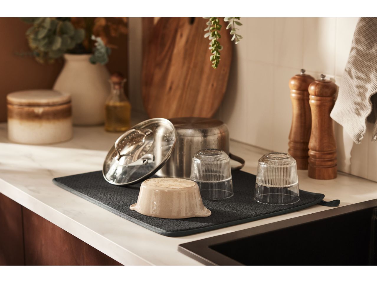 A dark gray drying mat holds various kitchen items, including glasses, a small bowl, and a pot lid.