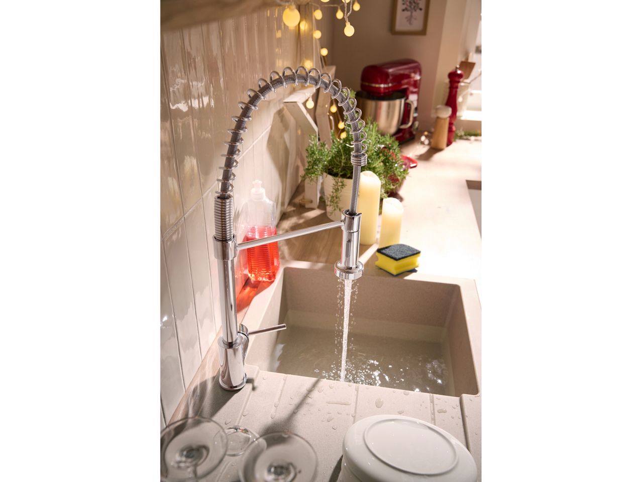 A kitchen sink with a modern faucet, running water, and festive lights.