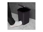 Foot operating a dark grey pedal bin with a woven texture, lid open, on a tiled floor.