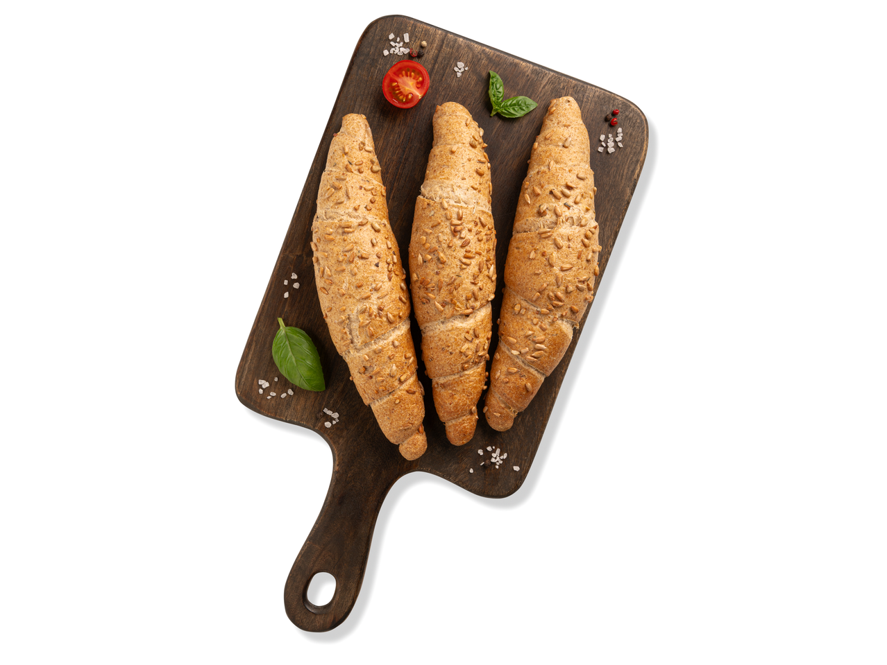 Három magvas teljes kiőrlésű stangli fa vágódeszkán, paradicsommal és bazsalikommal.