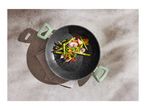 Black wok with green handles filled with stir-fried vegetables on a grey surface.