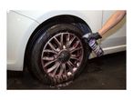 Hand in black glove spraying wheel cleaner on a car wheel, turning purple from dirt.