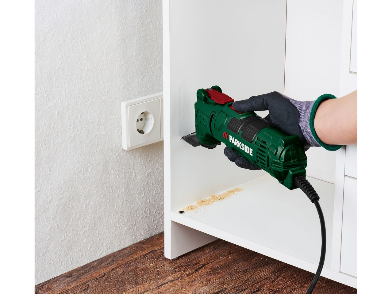 A person uses a multi-tool to sand the inside of a white cabinet, creating sawdust.