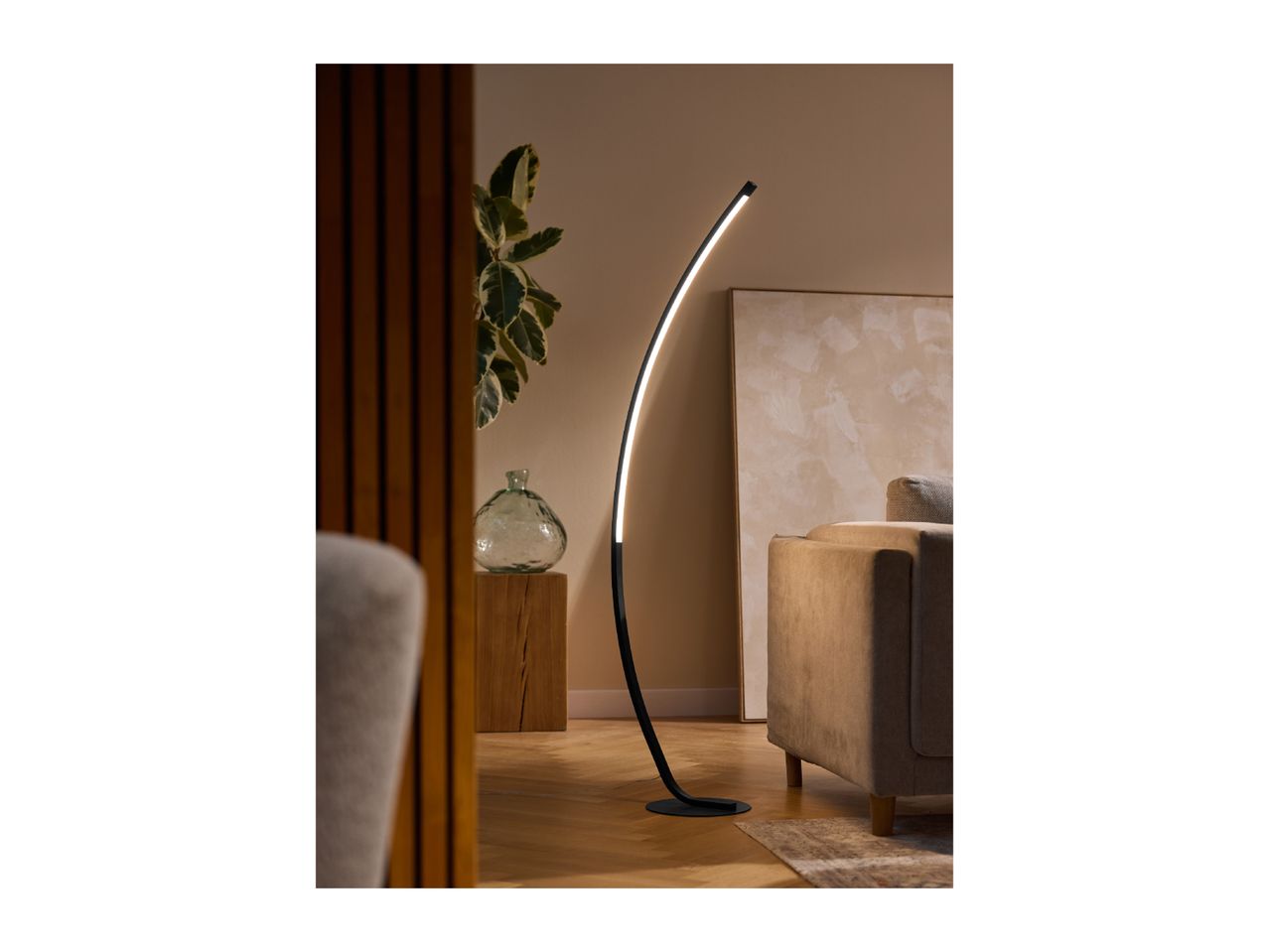 A modern black floor lamp with a curved design illuminates a living room with a beige sofa.
