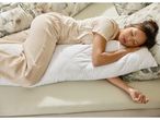 Una donna dorme di lato su un cuscino laterale per il corpo, indossando un pigiama color crema.