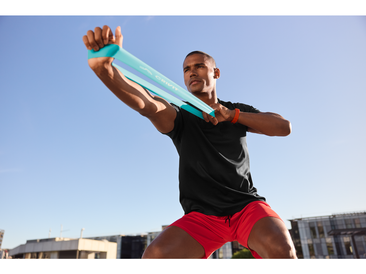 Man in CRIVIT sports shorts and t-shirt exercising with a resistance band.