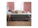 Woman sleeping on a dark grey mattress with a white top layer, next to a wooden nightstand.