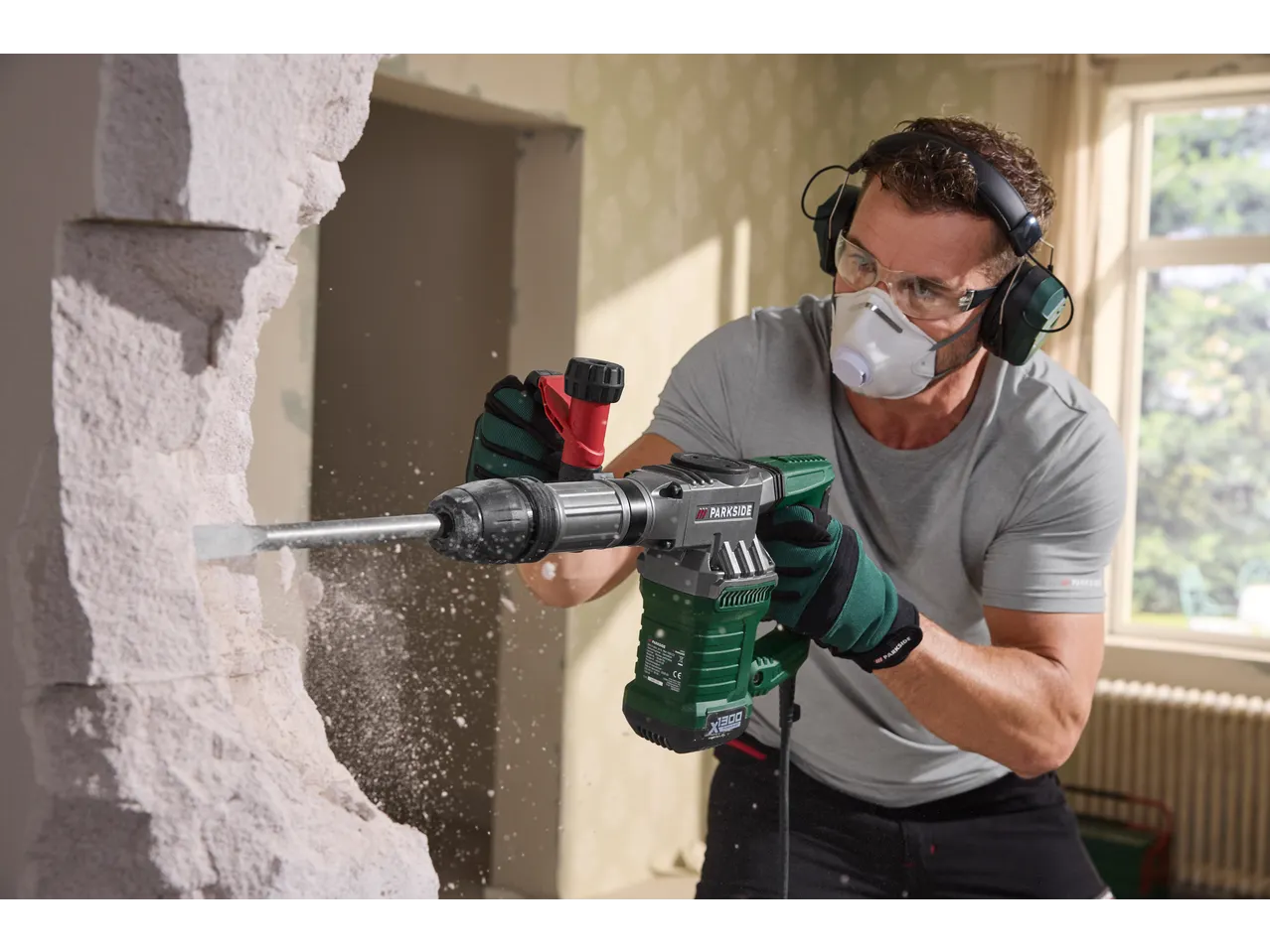 Homem usa martelo demolidor PARKSIDE com equipamento de proteção, demolindo parede.