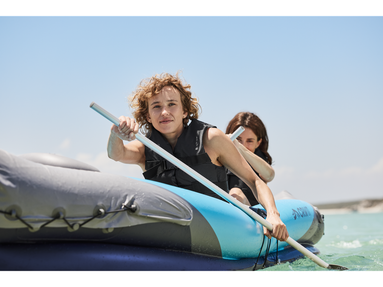 Two women paddle an inflatable Aclam kayak.
