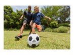 Father and son playing soccer in the garden, with a soccer ball in the foreground.