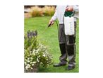 Person spraying plants in a garden with a pressure sprayer.