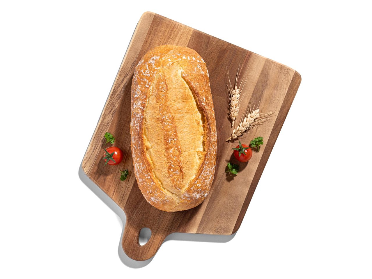 Friss, ropogós kenyér egy vágódeszkán, paradicsommal és búzakalásszal díszítve.