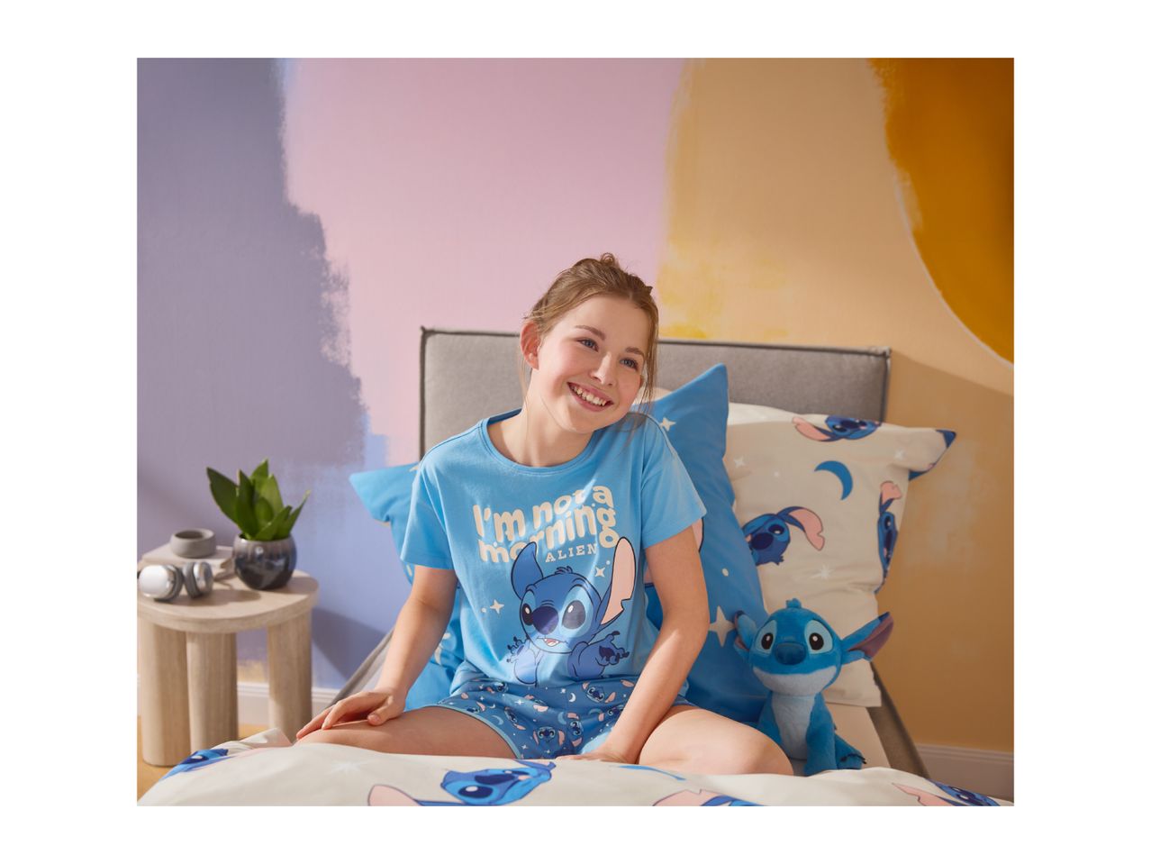 Girl in blue pyjamas with a cartoon character, sitting on a bed with matching bedding.