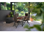 Outdoor dining set with a brown table and chairs, next to a black storage box, in a sunroom.