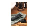 A black hair clipper and an attachment on a green towel, with bathroom accessories in the background.