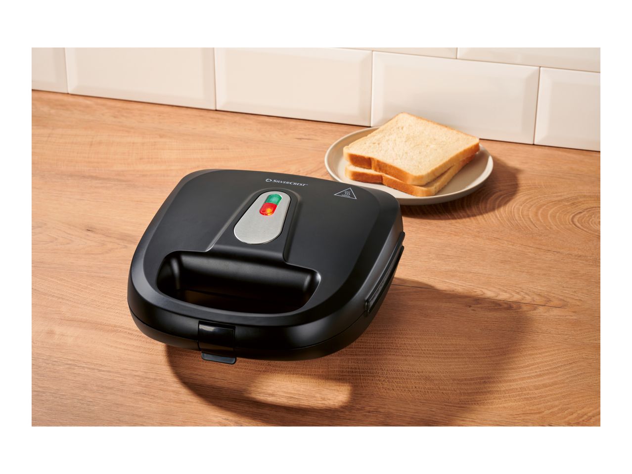 Black sandwich maker on a wooden counter with two slices of bread on a plate.