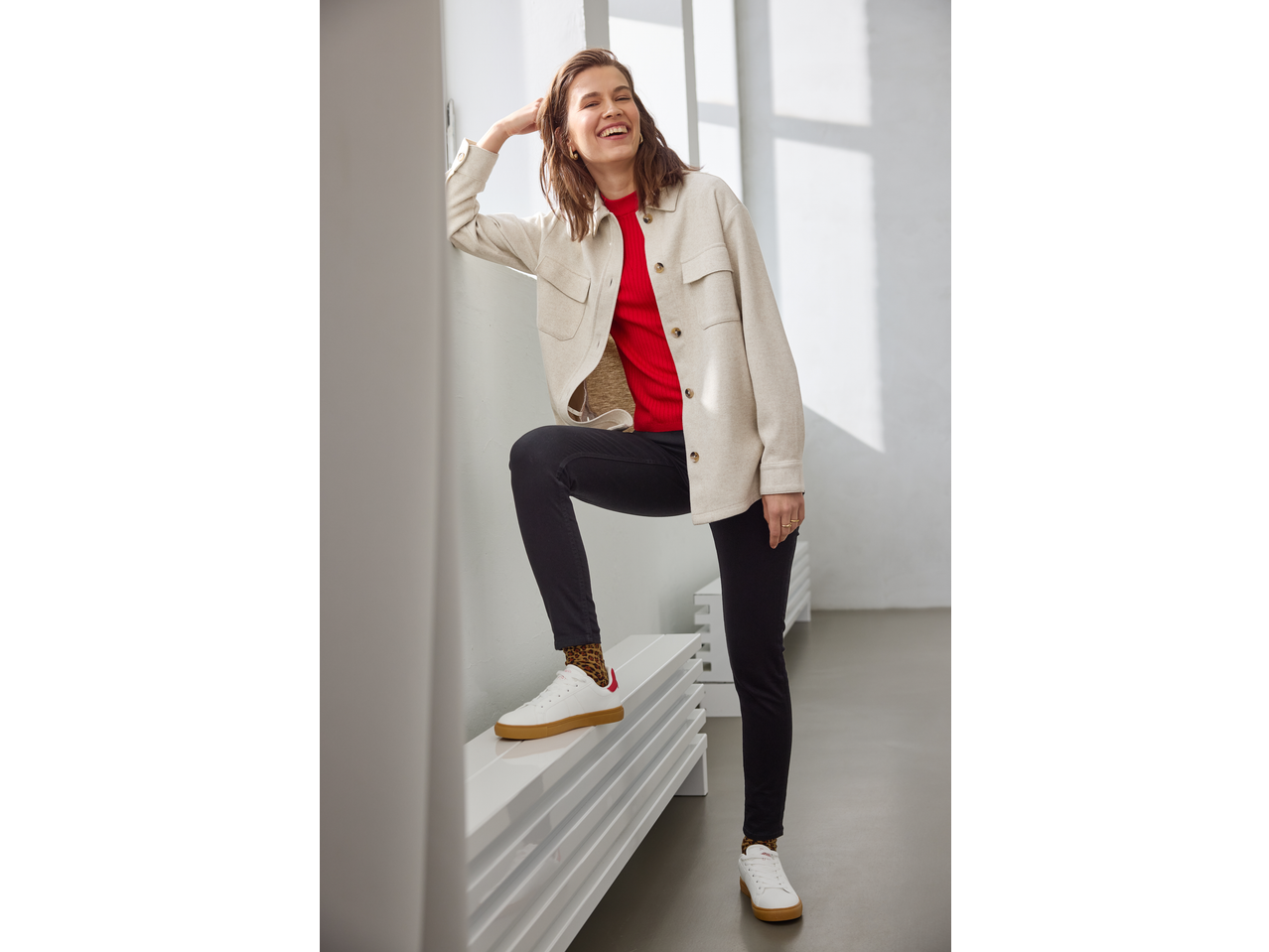 Smiling woman in an esmara® fleece overshirt, red top, black trousers, and white sneakers.